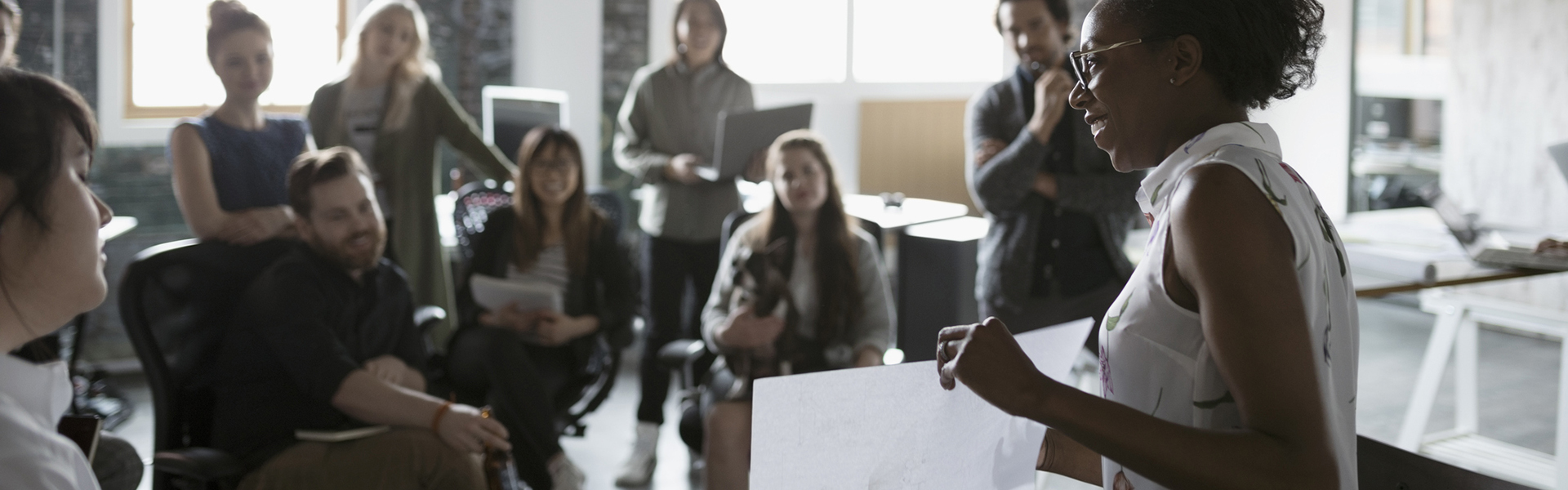 Female architect with blueprint leading meeting in open plan loft office