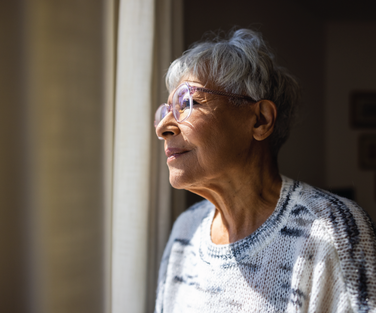 An elderly woman looks out a window