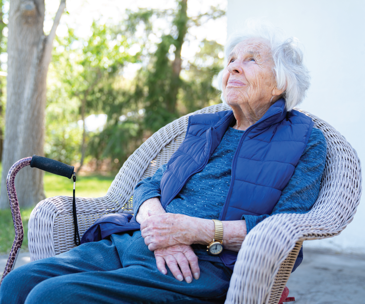 An elderly woman sits outside her home