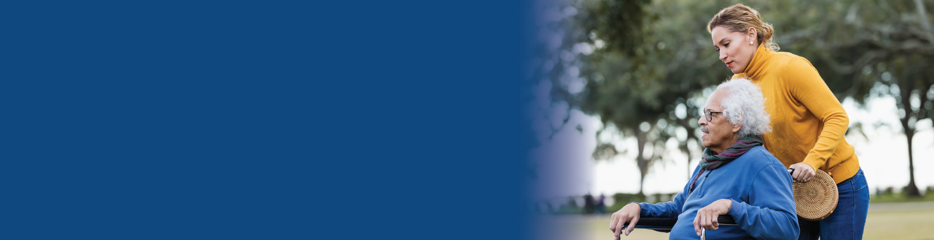 A woman pushes her elderly father in a wheelchair outside.