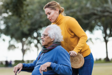 A woman pushes her elderly father in a wheelchair outside.