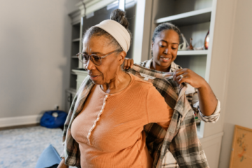 Caregiver helps older woman put on her jacket