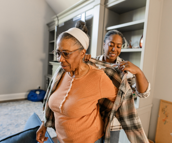 Caregiver helps older woman put on her jacket